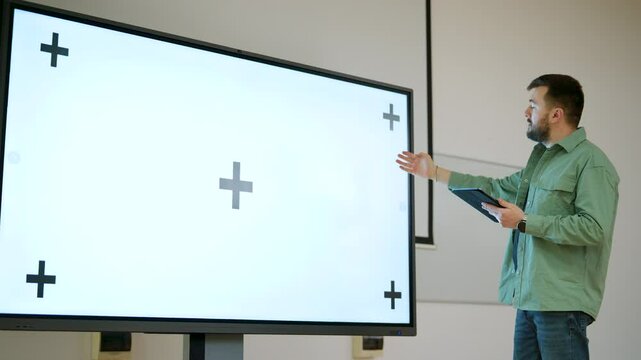 Man presenting in a spacious classroom using a large screen with a whitescreen and tracking points, ichroma key ready
