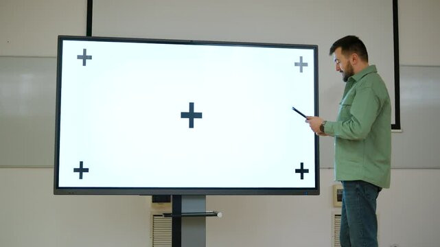 Man presenting in a spacious classroom using a large screen with a whitescreen and tracking points, ichroma key ready