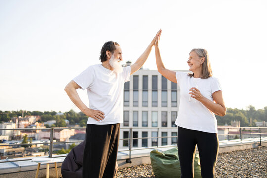 Elderly man and woman in casual clothing giving high five after rooftop morning exercise. Scene depicts smiles, fresh air, and healthy, happy lifestyle. Written to inspire positivity and activity.