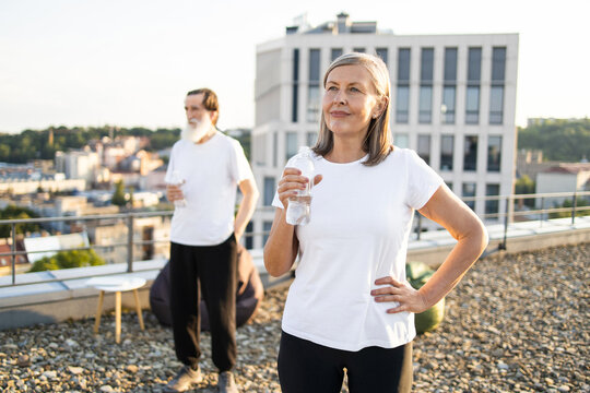 Senior man and woman taking a break outdoors, hydrating with water bottles, urban rooftop background. Enjoying healthy, active lifestyle and outdoor ambiance in scenic city environment. - Powered by Adobe