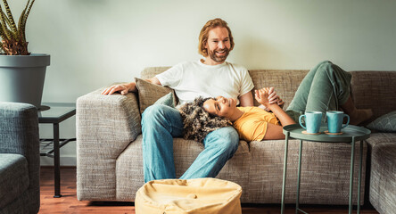 Cheerful multiracial couple sitting on sofa in the living room - Happy family moving in new home - Real estate and stylish furniture concept