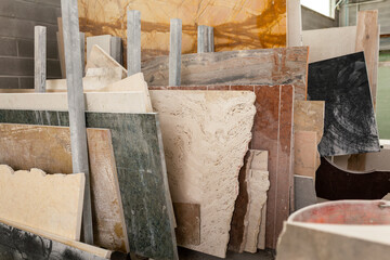 Various slabs of marble and stone in different colors and textures lean against each other in a workshop or warehouse.