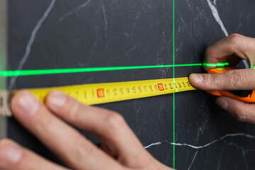 hands of a worker who measures the width of a tabletop with a tape measure and a laser