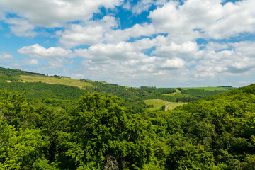 Vibrant green hills stretch beneath a vast sky filled with fluffy clouds in a serene countryside...