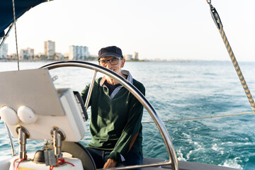 Senior skipper steering sailboat in coastal waters, enjoying maritime life