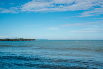 Obraz premium Tropical beach with calm blue sea, clear sky, and lush green island – perfect for travel, nature, and relaxation themes.