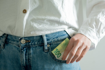 Close-up of hand putting 100 euro banknote into pants pocket