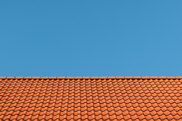 Naklejka premium Roof Under Azure Sky: A vivid scene showcasing the juxtaposition of a vibrant, red-tiled roof against a vast, clear, blue sky. The roof's texture.