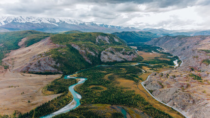 Aerial view of a turquoise river winding its way through a colorful autumnal valley, surrounded by...