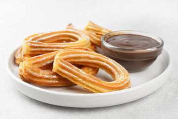 Traditional spanish dessert churros, fried dough pastry dusted with powdered sugar and chocolate sause on white background. Street food, sweet snack, homemade dessert. Top view, copy space