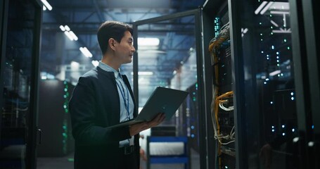 Asian Data Center Engineer Opening Server Cabinet in a Technological Facility. Specialist Using Laptop Computer Next to Server Hardware and Mainboard, Updating Network Options and Testing Connection
