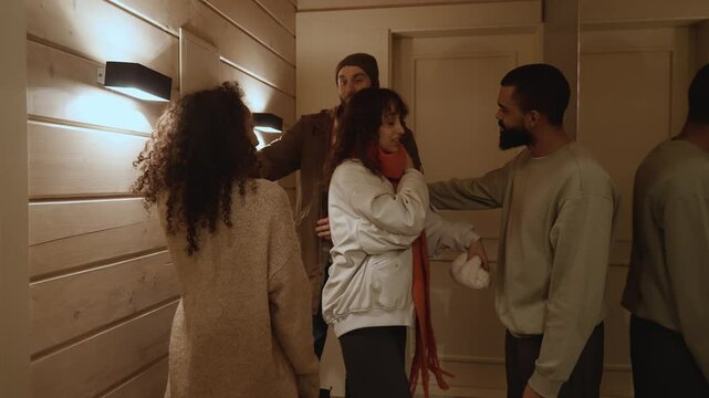 Two couples say goodbye to each other and hug while one stands in the hallway and the other leaves