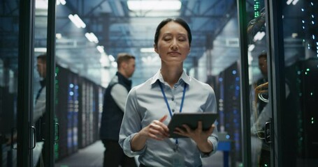Asian Female AI Engineer Using Tablet Computer while Walking Between Server Racks and Inspecting Hardware and Stable Connection. Colleague Pushing a Cart in the Background. Slow Motion Footage - Powered by Adobe