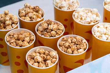 delicious sweet caramel brown popcorn. in a yellow orange glass close-up. boxes of popcorn on sale on the counter in the store. Paper cup with popcorn snack on the table