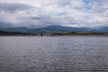 Concrete dam of the Liptovská Mara reservoir in Slovakia. Calm water, rocky shore, and mountain...