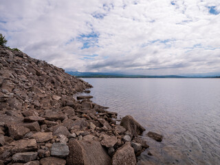 Rock-covered slope of the dam at Liptovsk&aacute; Mara reservoir in Slovakia. View of calm water surface, cloudy sky and distant hills.