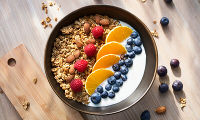 Top view of healthy breakfast with fresh fruits, granola, and yogurt on table in bright natural light, clean and minimal composition