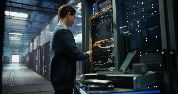 Asian Server Technician Installing Additional Hardware into a Server Cabinet in a Data Center. Focused Specialist Inserting Hard Drives in Order to Increase Storage, Memory and Compute Power