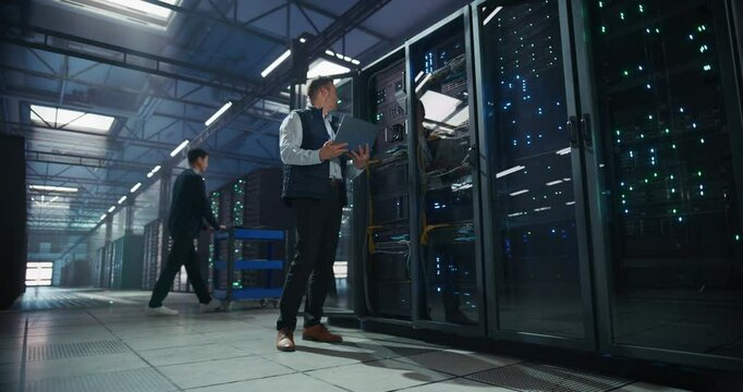 Software Developer Coming to Analyze System Performance Metrics on a Laptop Computer Inside a Modern Data Center. Technical Manager Inspecting Critical AI Hardware and Infrastructure