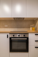 Front view of a modern kitchen cooktop and oven with white cabinets and wood countertop in neutral tones