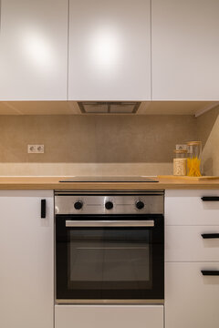 Front view of a modern kitchen cooktop and oven with white cabinets and wood countertop in neutral tones