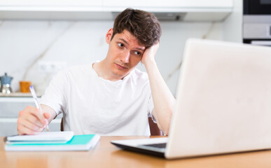 Upset man with laptop and utility bills in kitchen