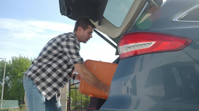 Man loading orange suitcase into car trunk before journey. Packing luggage for travel