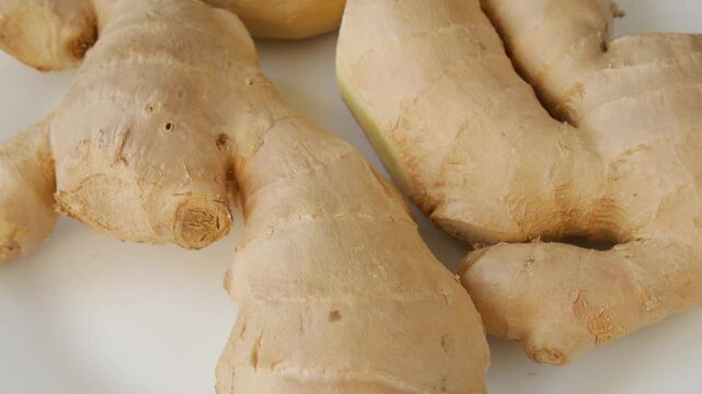 Ginger roots slowly rotating against pristine white background, revealing intricate texture, natural patterns, and vibrant organic quality of fresh rhizome.