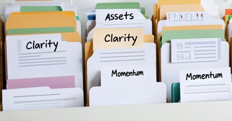 Colorful file folders, labeled with words like assets, clarity, momentum. Organization system suggests document storage, information retrieval.