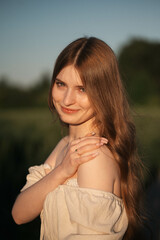 Fototapeta premium Elegant woman with long dark hair wearing a beige dress in a rural field at sunset, emotional close-up with warm backlight and soft tones, natural beauty in outdoor setting