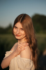 Fototapeta premium Elegant woman with long dark hair wearing a beige dress in a rural field at sunset, emotional close-up with warm backlight and soft tones, natural beauty in outdoor setting