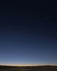 Fototapeta premium Night sky over desert landscape astrophotography showing stars constellations and horizon in dark blue and brown tones