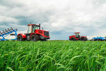 Obraz premium a red tractor on a green field against a blue sky background. The concept of harvesting and tillage in summer or spring. Agriculture. Machinery. Farming machinery.