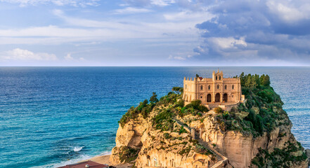 sea landscape of beautiful white temple or castle on a high cliff isle on a rock in crystal clear turquoise sea with waves and beautiful sunset or sunrise on background of seascape