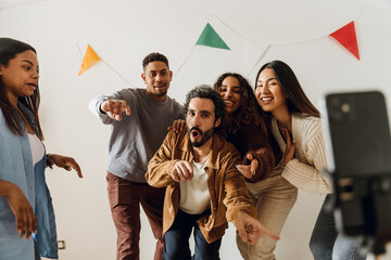 Young brown-skinned male and female friends enthusiastically record an entertaining video with a smartphone, dancing and singing. A concept of partying, togetherness, and friendship.