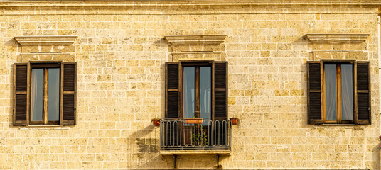old yellow facade of house with three brown vintage wooden windows in retro italian european style