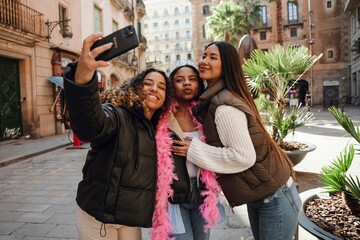 A multinational group of young women taking a cheerful outdoor selfie during a birthday party,...
