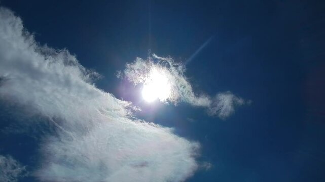 Blue sunny sky, sun, moving white clouds with colorful Cloud iridescence, Irisation with pearl colors and birds in flight. Topics: heaven, beauty of nature, sun energy, optical phenomenon, weather