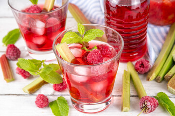Raspberry rhubarb iced tea, lemonade or mojito. Cold summer fruit refreshment drink with rhubarb syrup, raspberry and mint, on white wooden table 