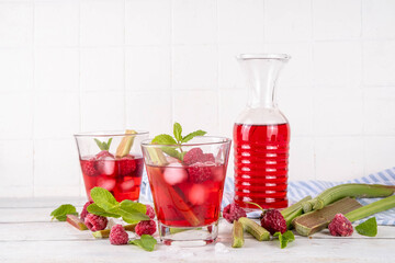 Raspberry rhubarb iced tea, lemonade or mojito. Cold summer fruit refreshment drink with rhubarb syrup, raspberry and mint, on white wooden table 