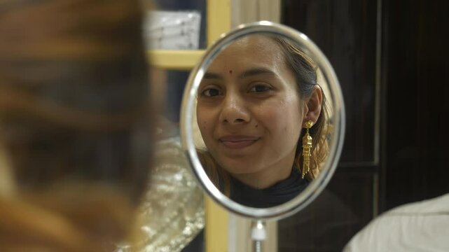 Young beautiful asian woman wearing designer 18k HUID certified gold earrings, looking at mirror and smiling