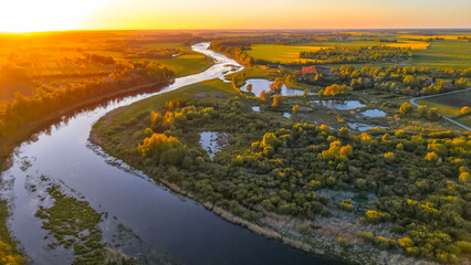 Aerial view of winding river and wetlands at sunset Drone image showing a meandering river, wetlands, and green landscape illuminated by golden sunset.