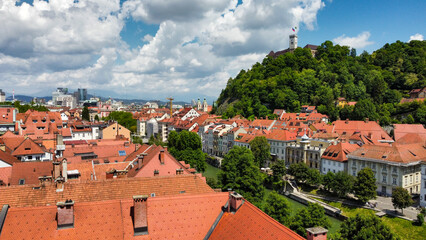 Obraz premium Aerial view of Ljubljana city center, Slovenia, showing red rooftops, the Ljubljanica River, and the iconic Ljubljana Castle atop the lush green hill.