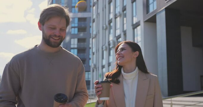 Cheerful couple walking through the city together. Couple drinking take away coffee after work. Smiling friends talking on street.