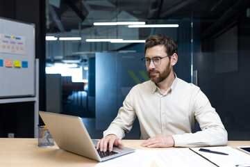 Serious and focused young man working in the office at a desk with a laptop