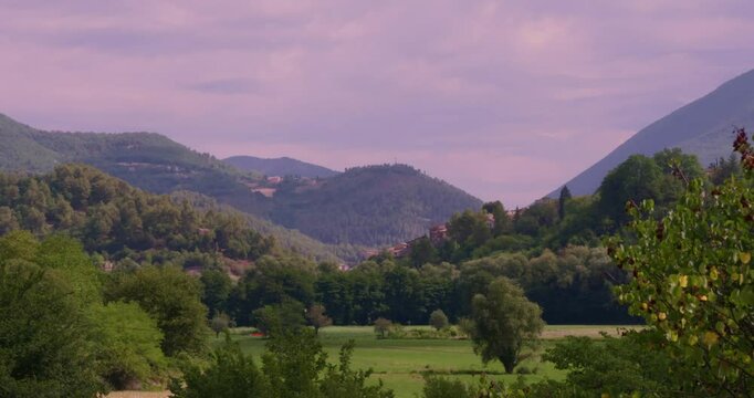 A wide shot of a lush Provence landscape in France, featuring rolling hills, dense forests, and open fields under a pastel sky with scattered clouds at dusk.