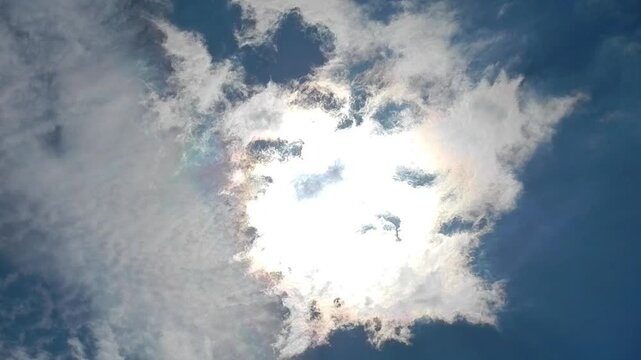 Blue sunny sky, sun, moving white clouds Altocumulus and Cirrocumulus with colorful Cloud iridescence, Irisation with pearl colors. Topics: heaven, beauty, sun energy, optical phenomenon, weather