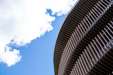 Modern architectural building with curved wooden facade and slatted design, under a bright blue sky...