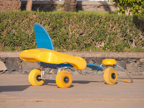 A bright yellow beach wheelchair with large wheels sits on a wooden boardwalk, ready for use. This specially designed chair enhances access for individuals wanting to enjoy the beach.