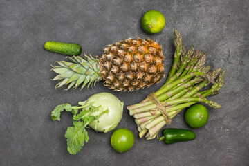 Pineapple and green asparagus tied in bunch on table. Kohlrabi, savoy cabbage and lime